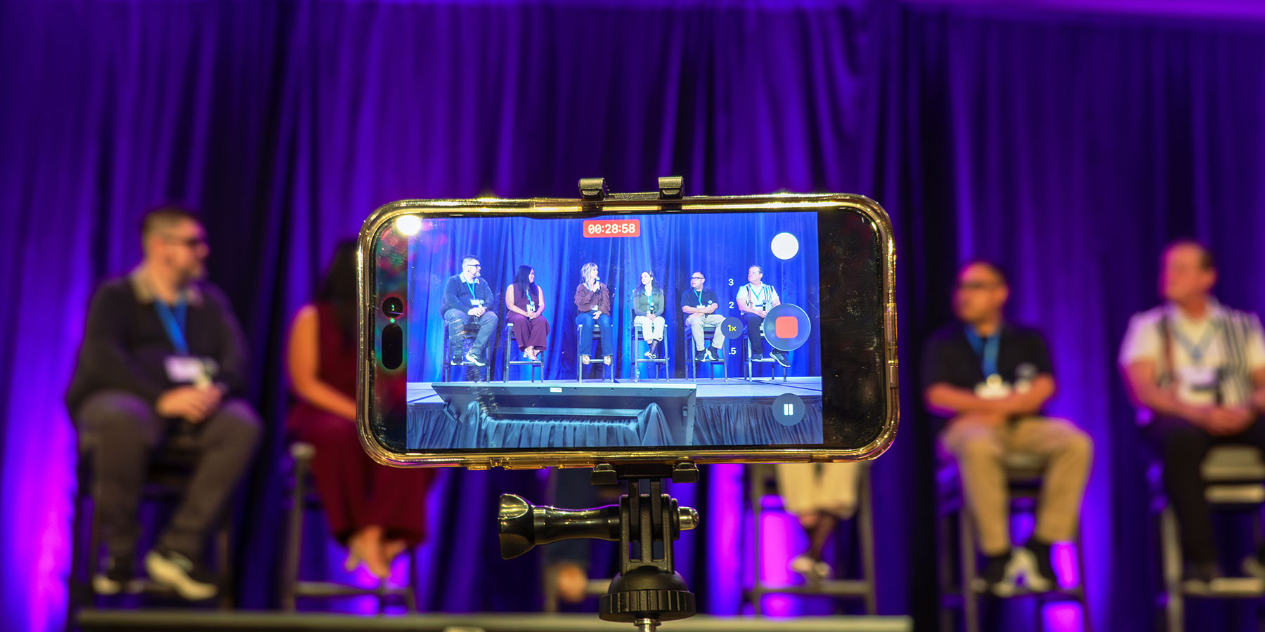 A smartphone records a panel of people on stage at the Direct to Consumer Wine Symposium, with purple curtains in the background.