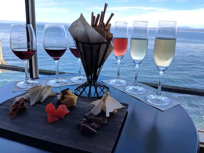 A wine flight and cheese board on a table overlooking the ocean.