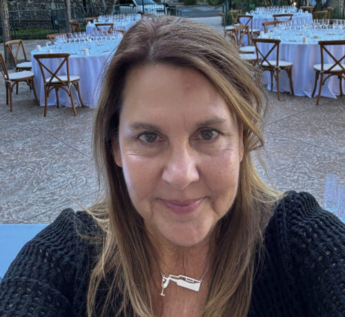 Woman smiling for a selfie outdoors with round tables and chairs set up in the background.