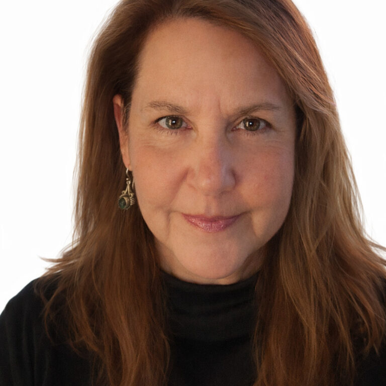 Woman with long, light brown hair and earrings, wearing a black top, smiling slightly at the camera.